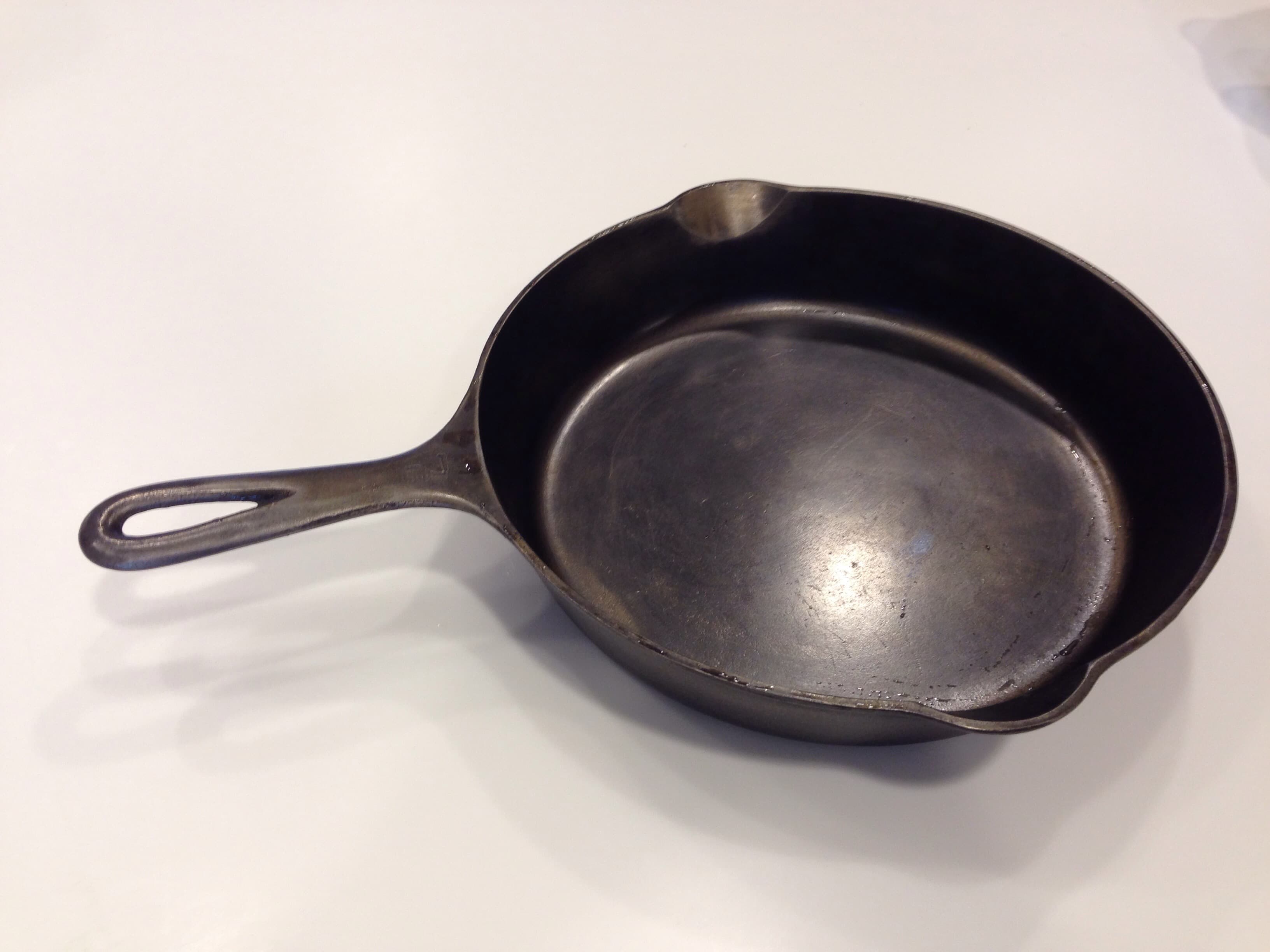 A seasoned cast iron skillet with a pour spout and long handle